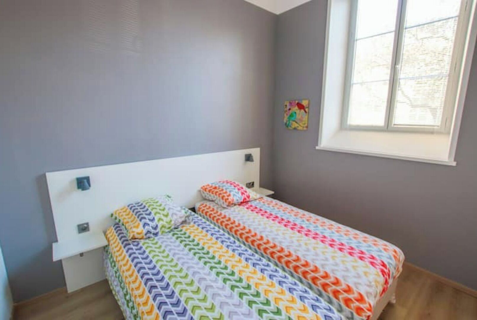 A bedroom with a bed, a window, and a wall-mounted artwork.