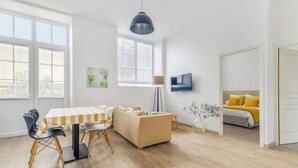 A modern living room with a dining area, a sofa, a TV, and a bed with yellow bedding. - La Maison D'olivier Avec Piscine Privatif (Mesnard-la-Barotière)