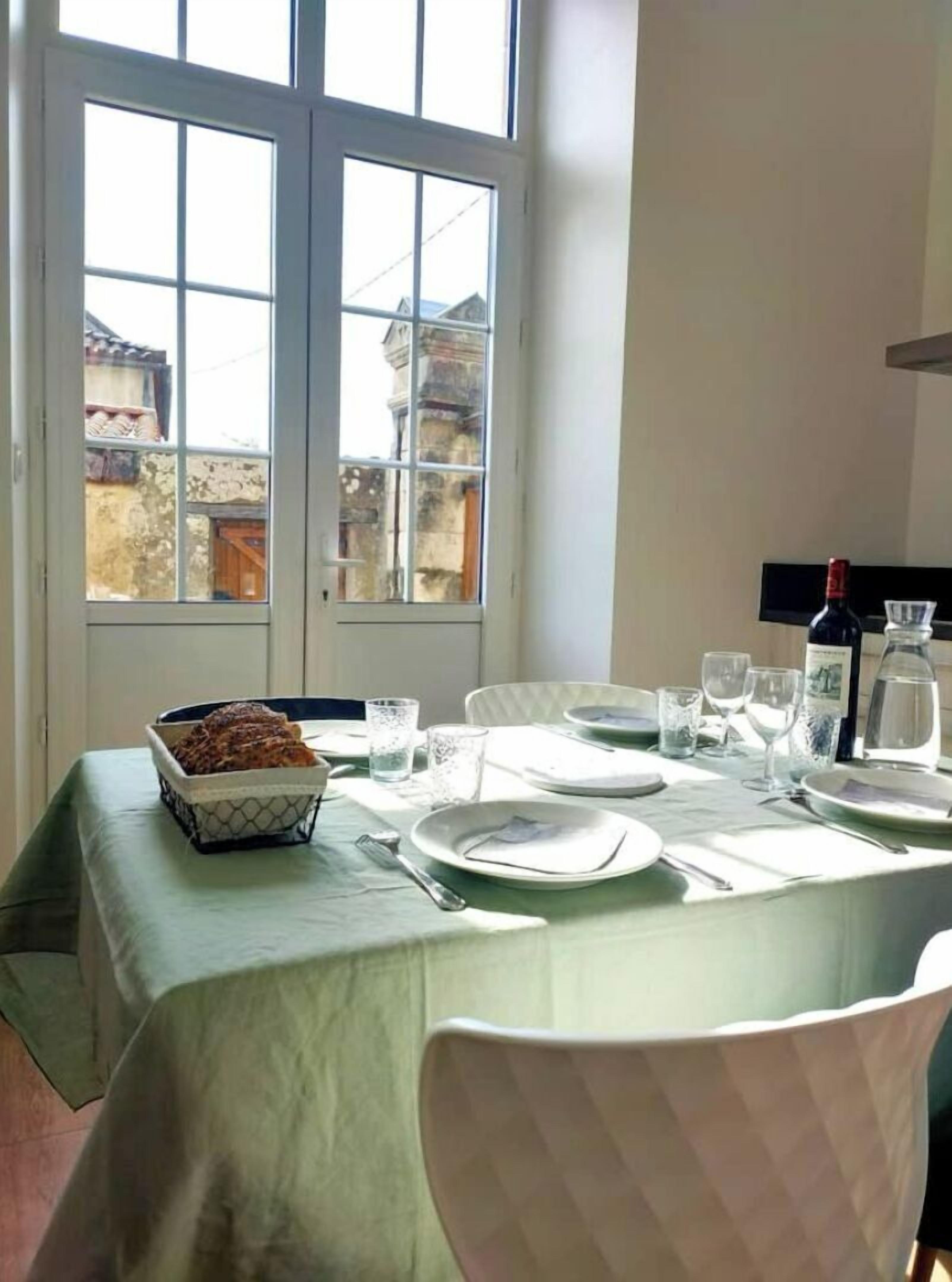 A dining table set for four with a bowl of bread, plates, cutlery, glasses, and a bottle of water.