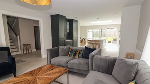 Un salon moderne avec un canapé d’angle gris, une table basse en bois et une cuisine en arrière-plan.