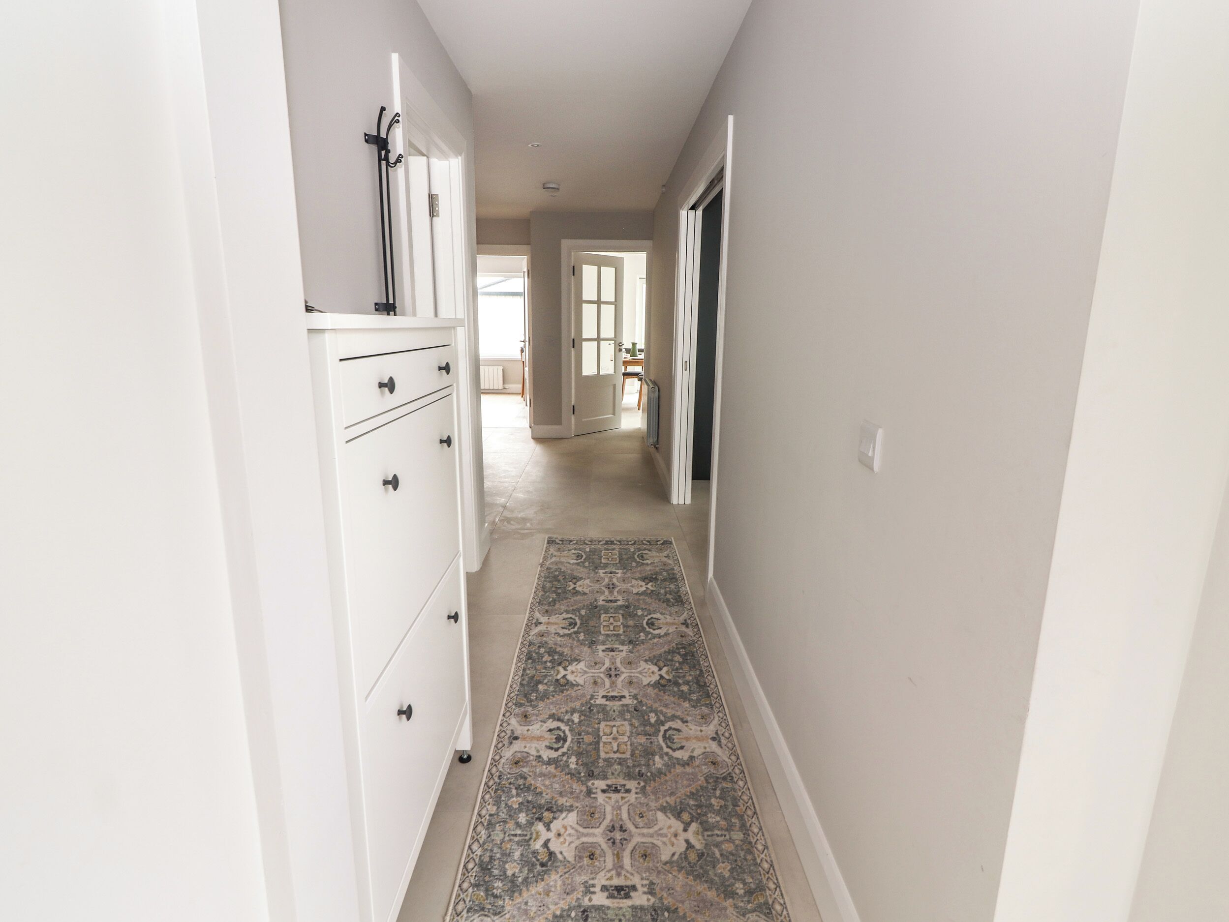 Un pasillo estrecho con un tapete estampado, armarios blancos y una puerta que da a otra habitación.