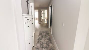 Un pasillo estrecho con un tapete estampado, armarios blancos y una puerta que da a otra habitación.