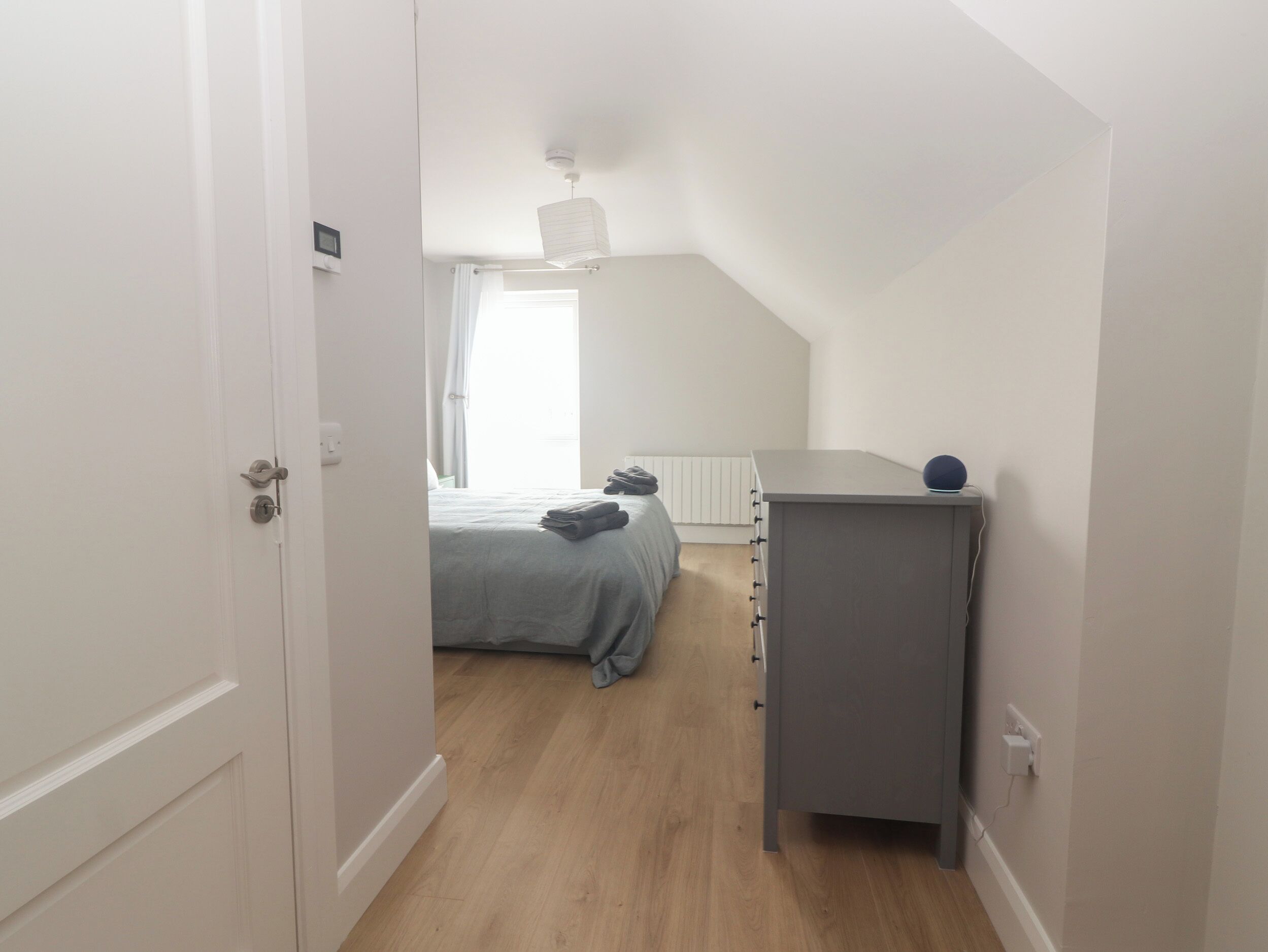 Un corridoio stretto che conduce a una camera da letto con un letto, una cassettiera e una lampada a soffitto.
