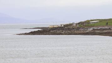 A coastal area with rocky shores, a small building, and a grassy hill.