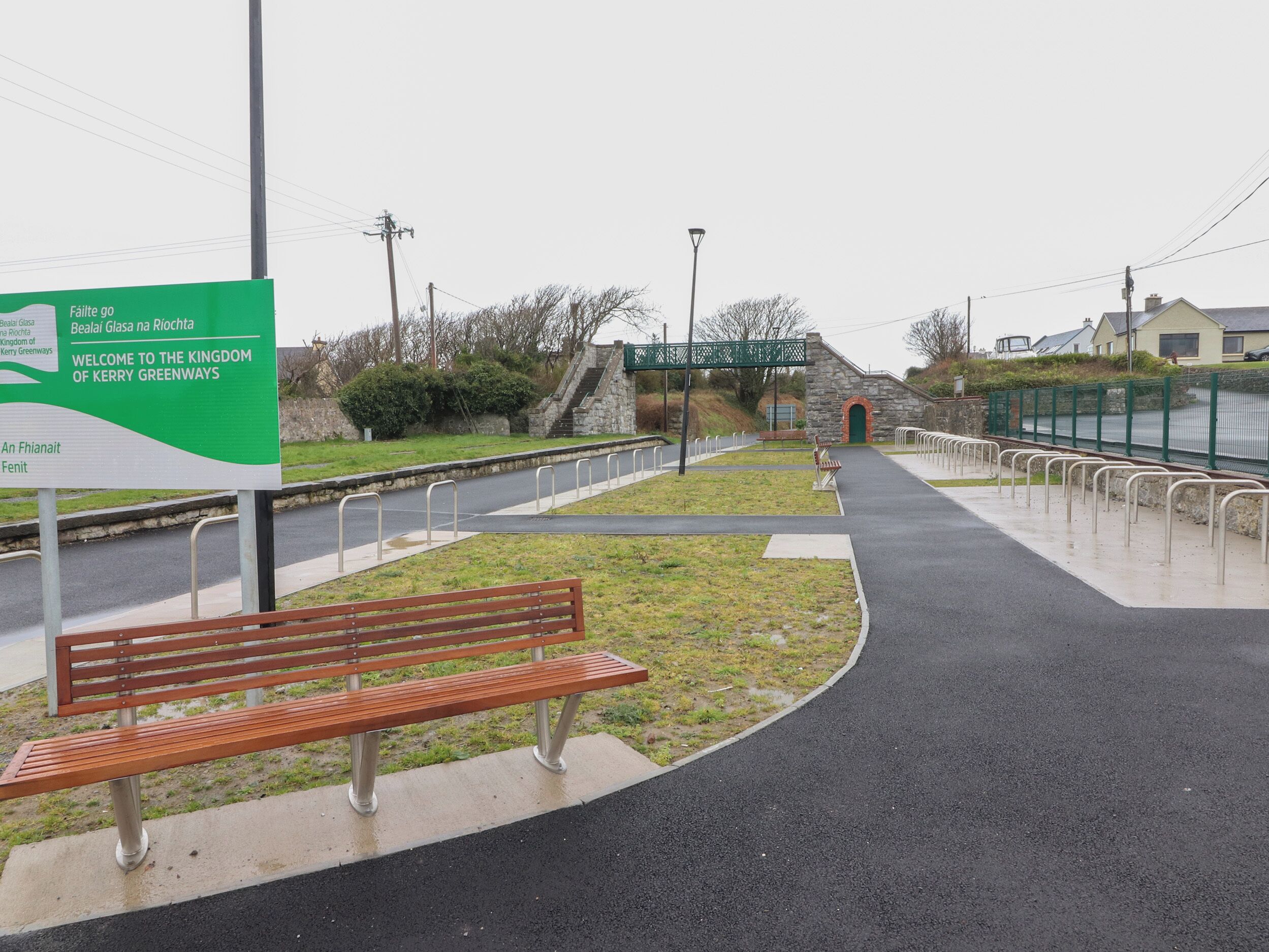 A pathway with a bench, a stone building, and a sign welcoming to the Kingdom of Kerry Greenways.