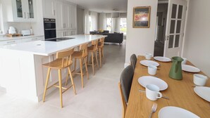 Une cuisine moderne avec des meubles blancs, un grand îlot central doté de tabourets de bar et un coin repas avec une table en bois pour quatre personnes.