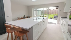 Une cuisine moderne dotée d’un grand îlot central, de tabourets de bar en bois et d’une porte vitrée donnant sur une terrasse avec vue sur le jardin.