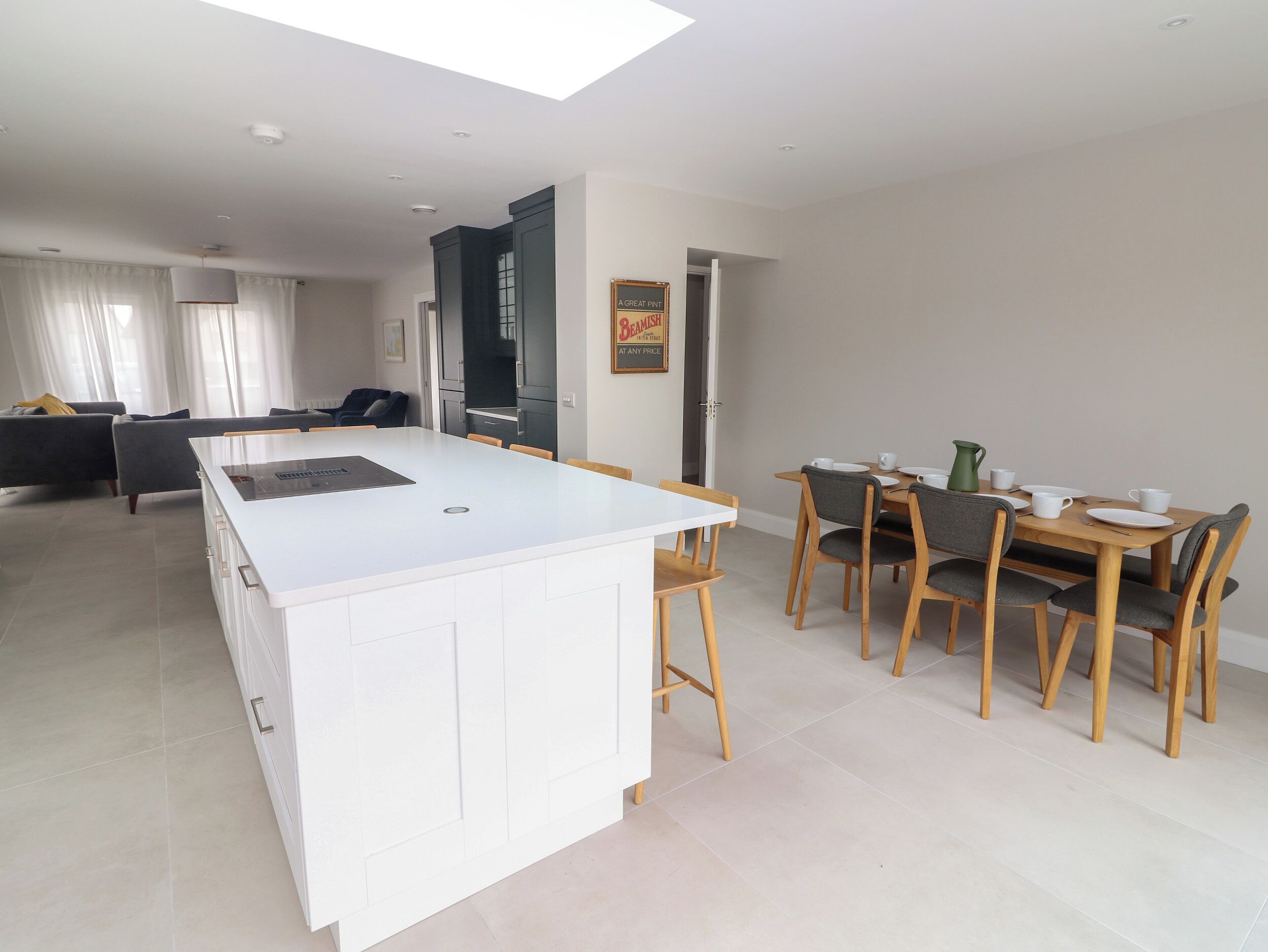 Eine moderne Küche mit einer zentralen Kochinsel, ein Essbereich mit Holzkästen und ein Wohnzimmer mit einer Couch und Vorhängen.