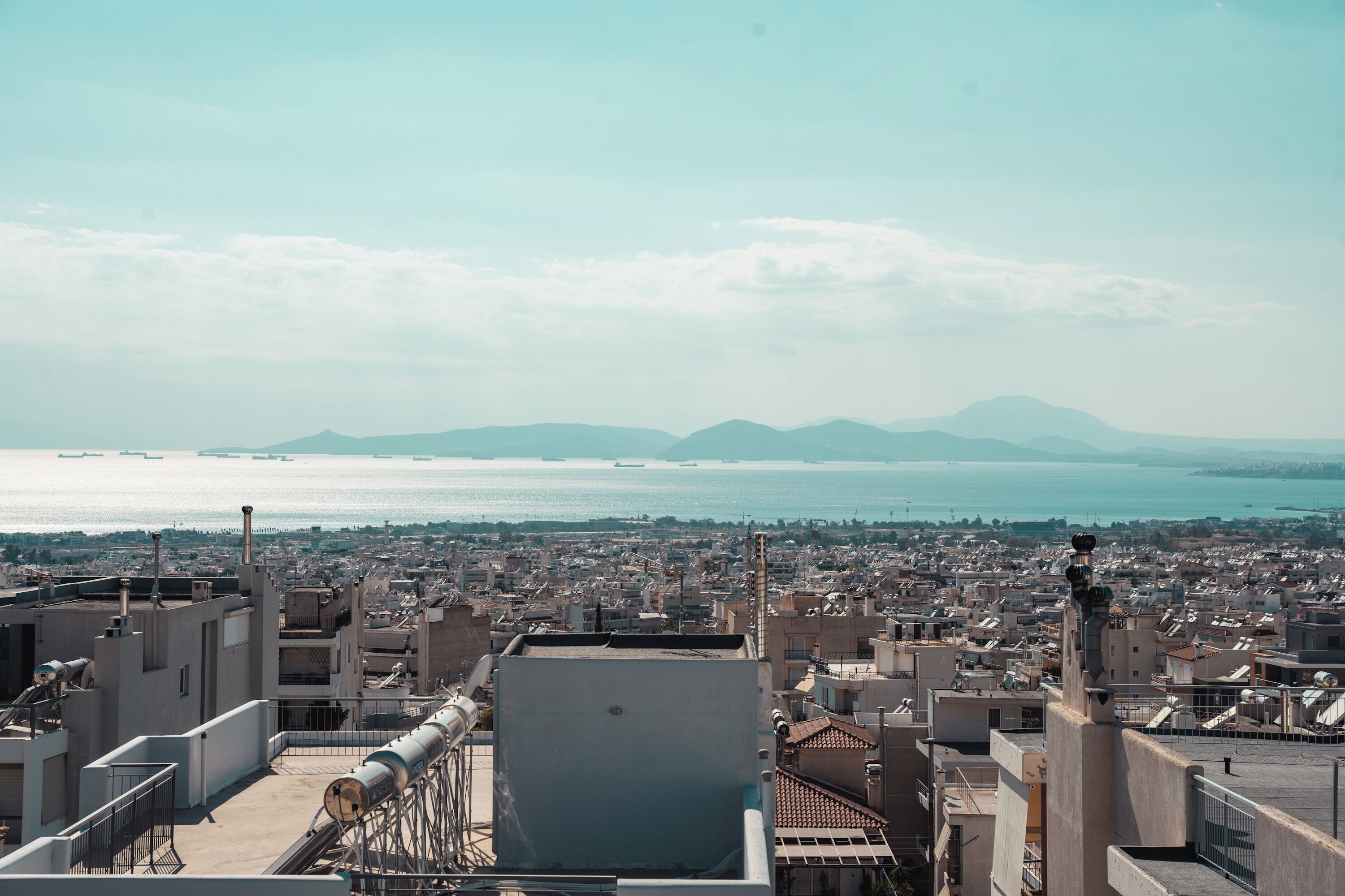 A cityscape with a view of the sea and mountains in the distance.