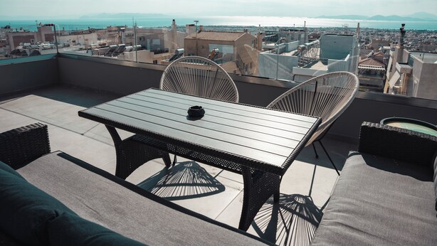 A rooftop terrace with a table and chairs, overlooking a cityscape and the sea.