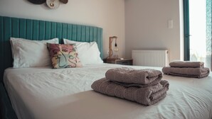 A neatly made bed with pillows and folded towels, a teal headboard, and a wall-mounted air conditioner.