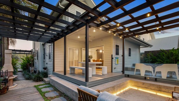 A covered patio with outdoor furniture, a barbecue grill, and a stone pathway.
