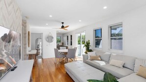 A modern living room with a sofa, a dining table with chairs, a TV, and a ceiling fan.