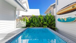 A swimming pool with a tiled edge, surrounded by white walls and green plants.