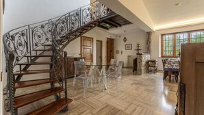 Amplia sala de estar con una escalera de madera, sillas de plástico transparente, una mesa de comedor y una chimenea.