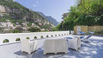 Une terrasse sur le toit, meublée de mobilier en osier, offrant une vue sur une ville côtière et s’ouvrant sur un paysage montagneux.