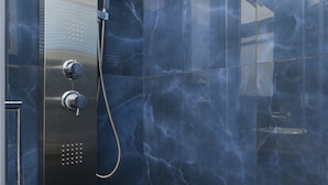 Une salle de bain moderne dotée d’une douche à parois de verre, de murs en marbre et d’un panneau de commande métallique.