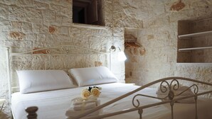 A bedroom with a stone wall, a metal bed frame, white bedding, and a small window. - Quattroperle Trulli - Relax - Puglia Private Pool (Puglia)