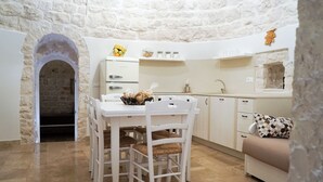 A compact kitchen with a stone archway, white cabinetry, and a dining area with white chairs. - Quattroperle Trulli - Relax - Puglia Private Pool (Puglia)