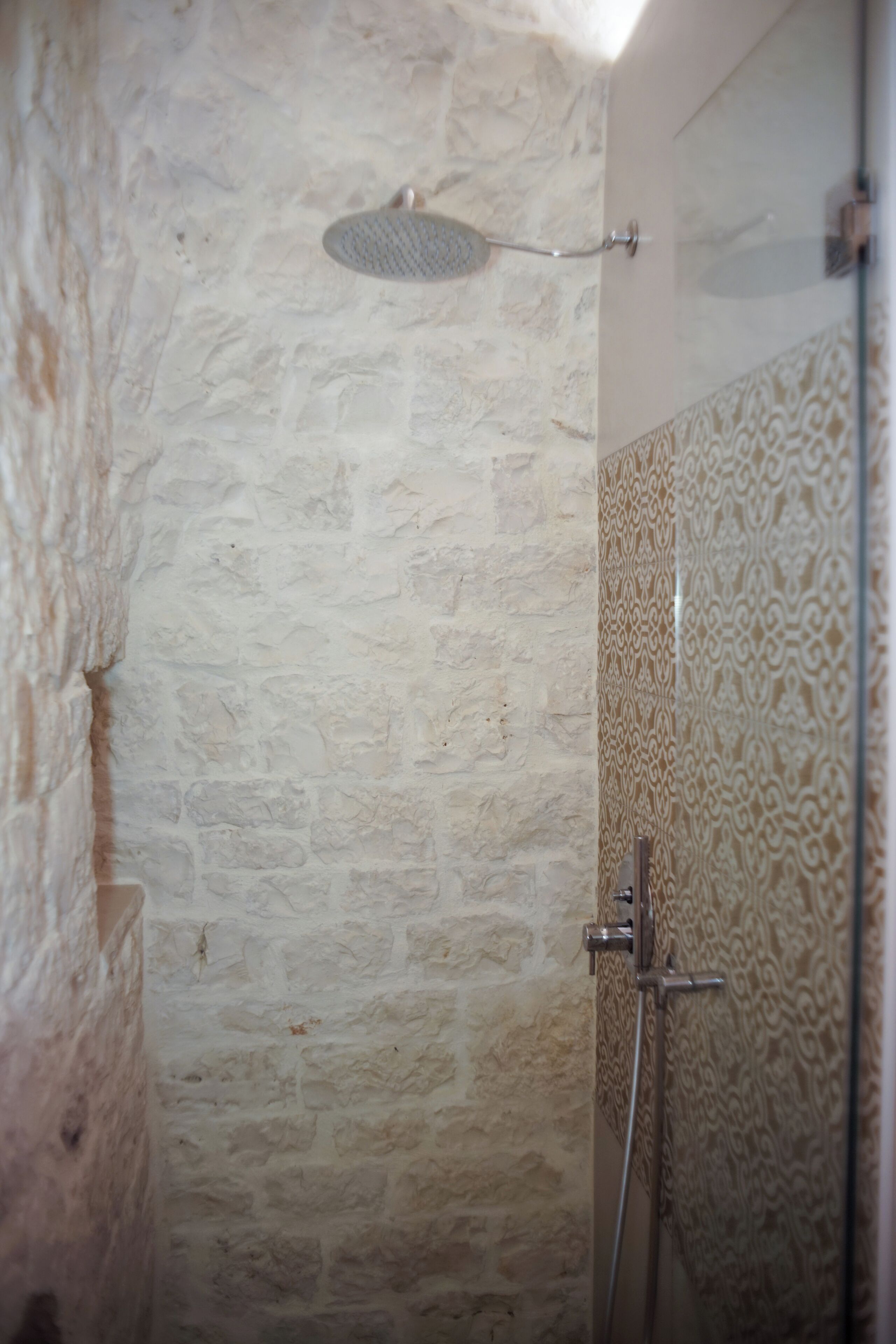 A shower with a stone wall and patterned tiles.