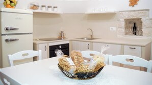 A kitchen with white cabinets, a white refrigerator, and a white dining table with a basket of bread. - Quattroperle Trulli - Relax - Puglia Private Pool (Puglia)