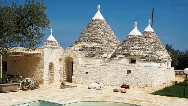 A swimming pool with stone buildings in the background. - Quattroperle Trulli - Relax - Puglia Private Pool (Puglia)
