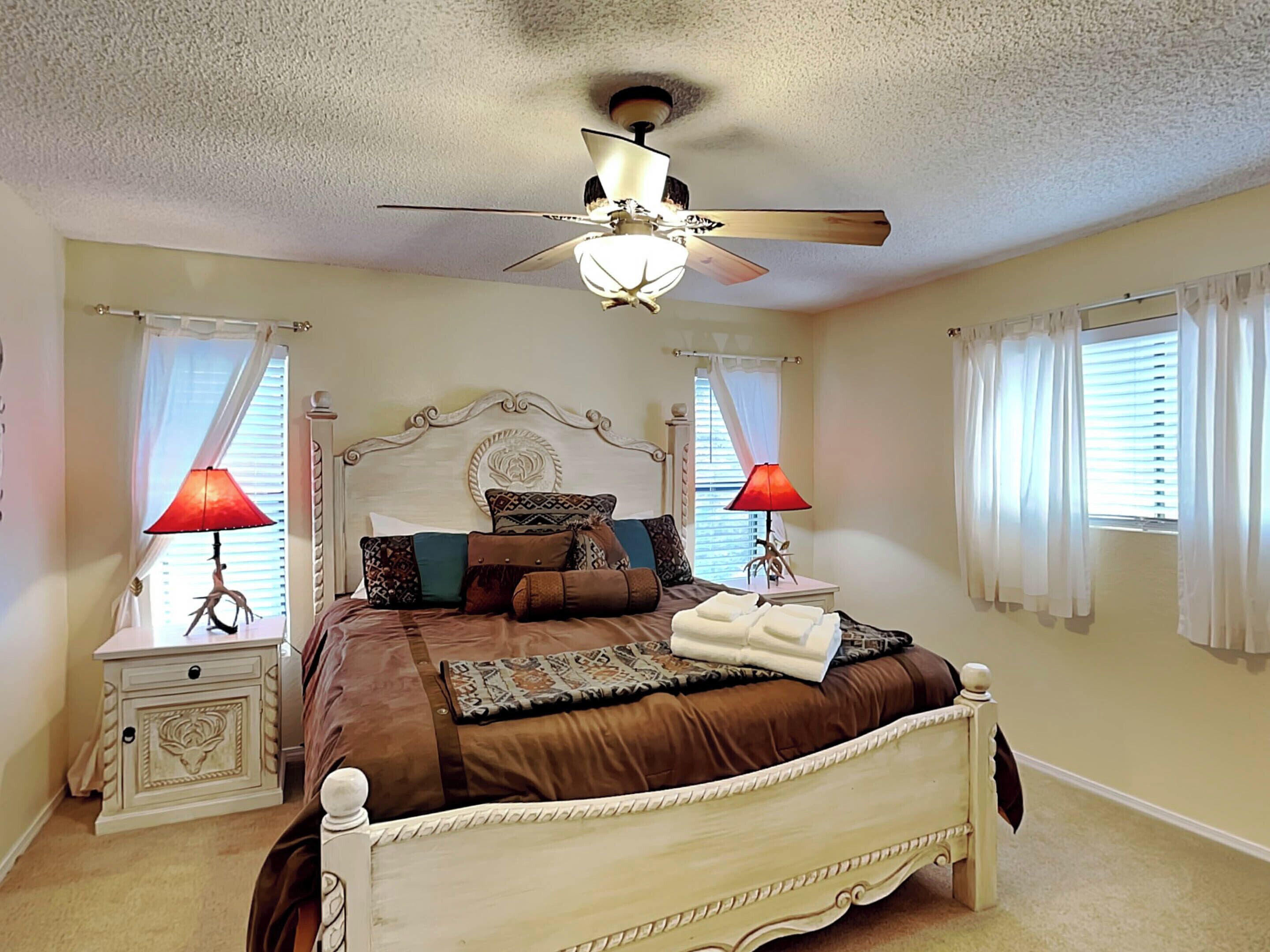 A bedroom with a bed, two bedside tables, a ceiling fan, and curtains.