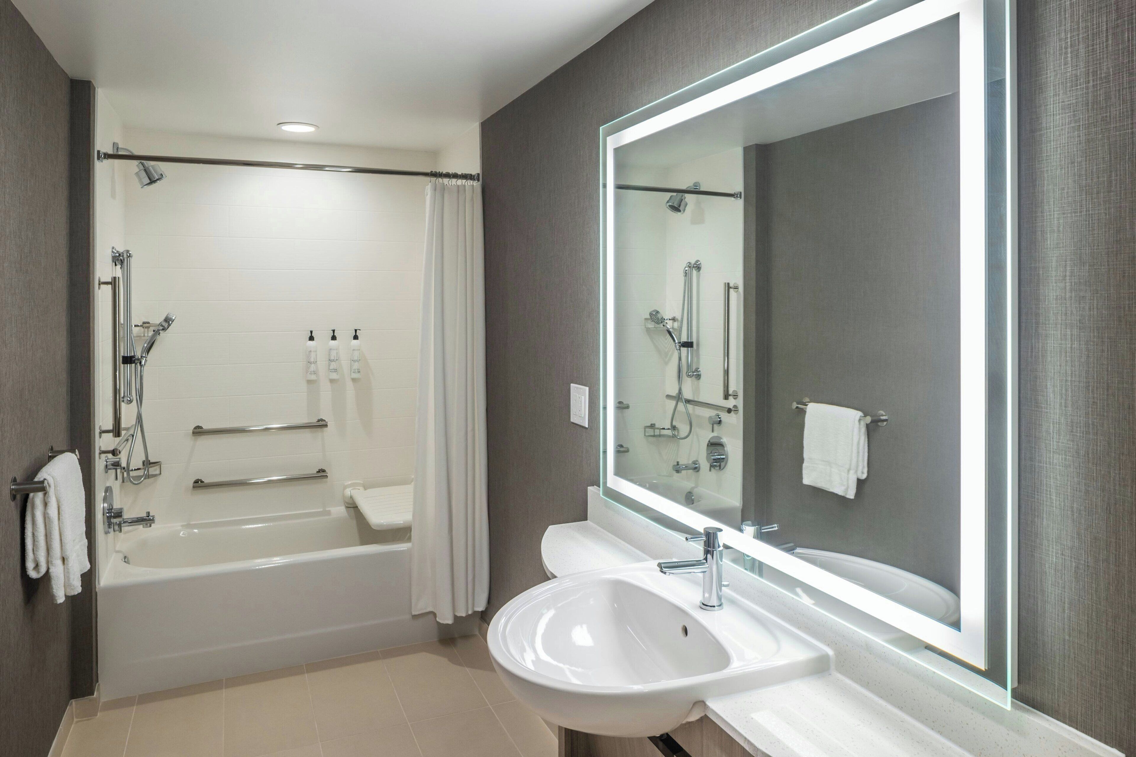 A modern bathroom with a bathtub, a large mirror, and a sink.