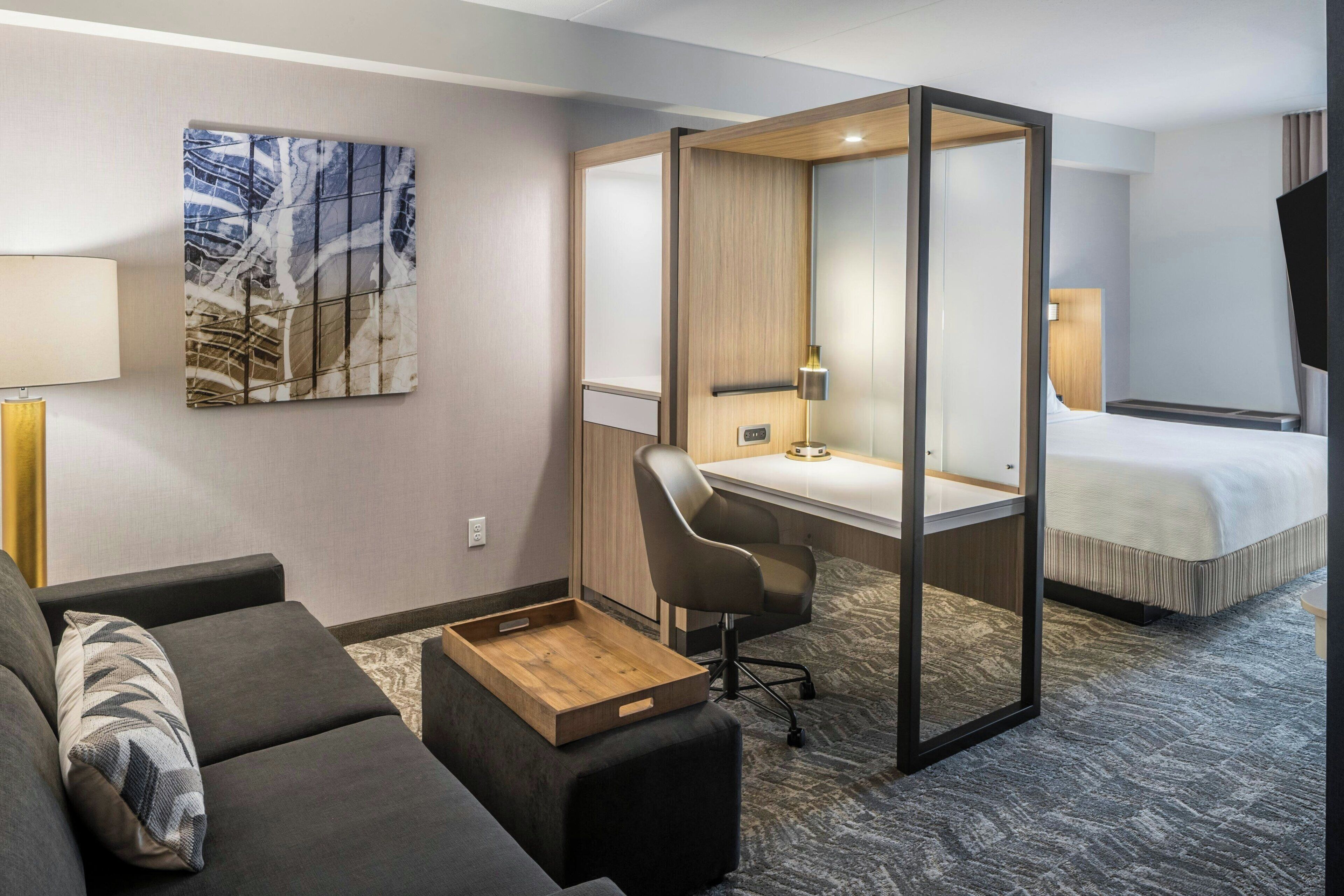 Une chambre d’hôtel avec un lit, un bureau, une chaise, un canapé et un tableau au mur.