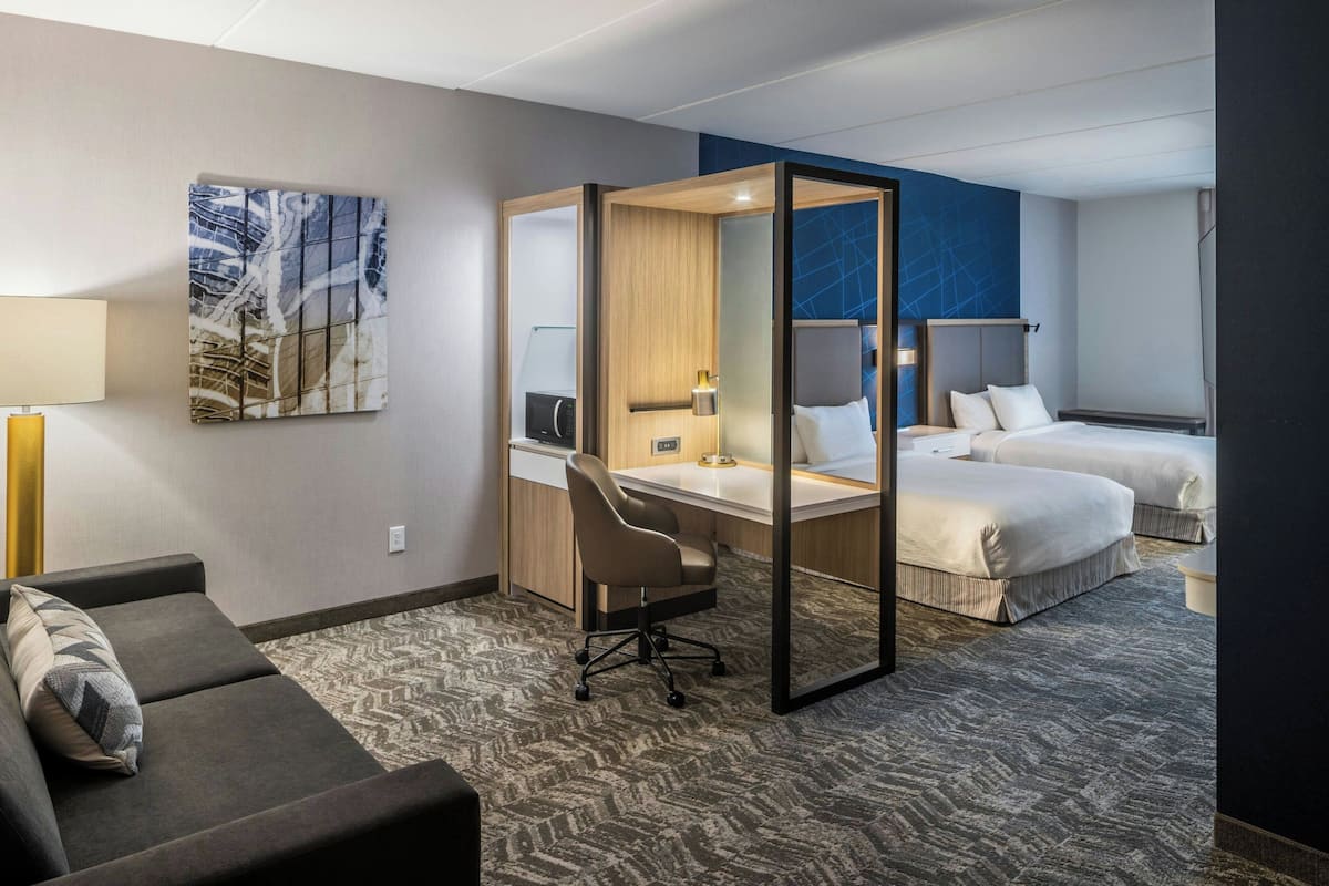 A hotel room with a desk, two beds, a sofa, and a large abstract painting on the wall.