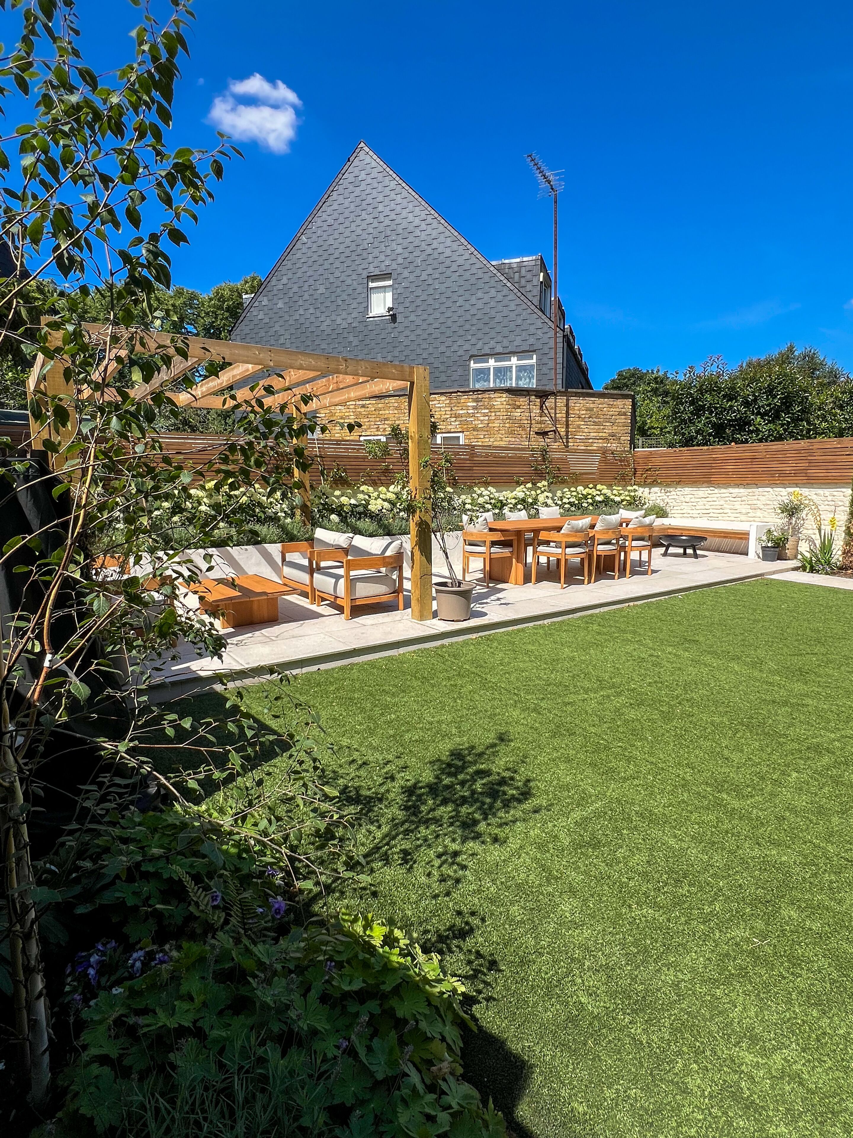 Een achtertuin met een houten pergola, buitenmeubels en een verzorgd gazon.
