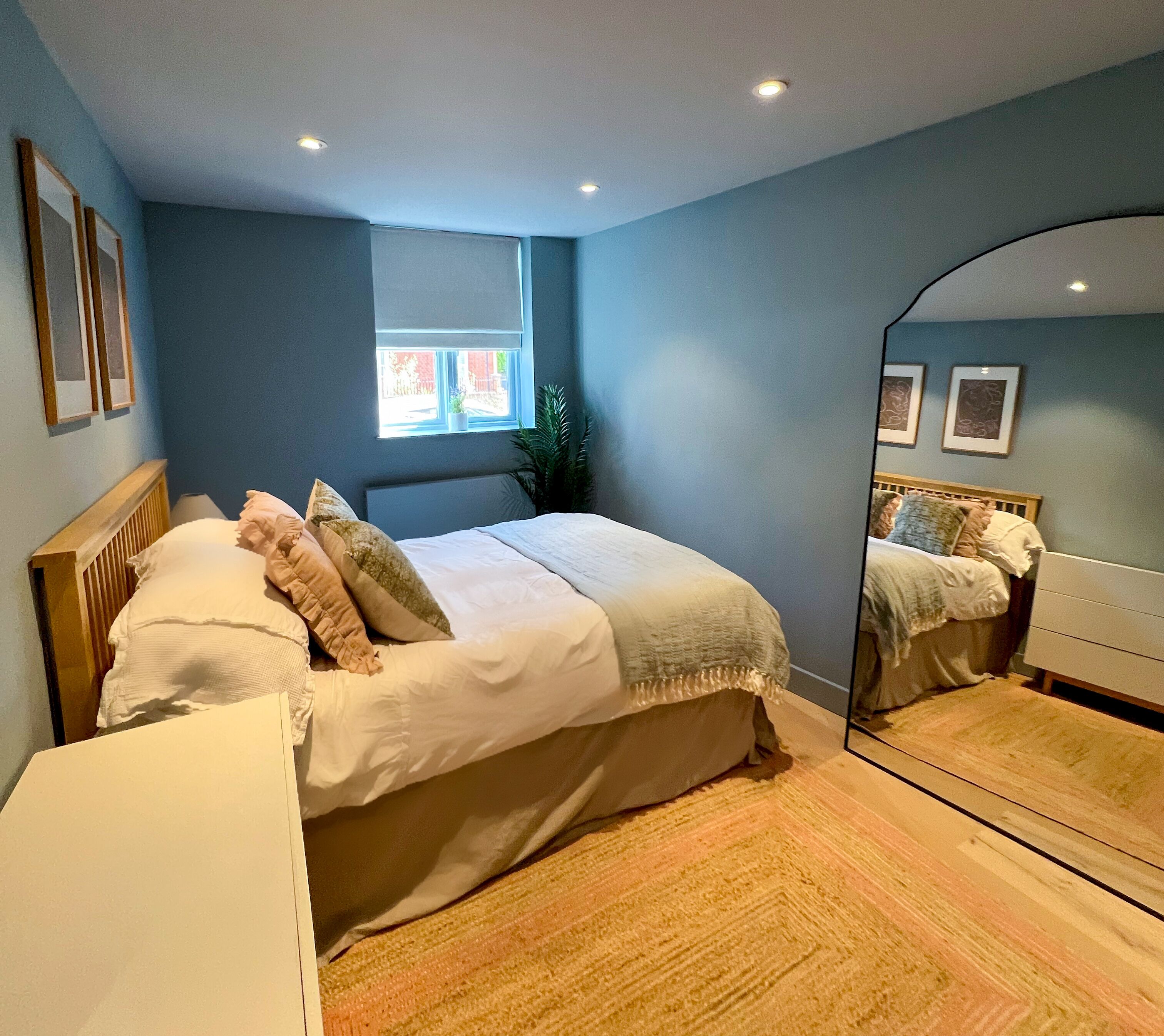 A bedroom with a bed, a mirror, a window, and a radiator.