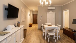 A modern kitchen with white cabinetry, a dining table with chairs, a chandelier, and a flat-screen TV mounted above the counter. - Appartamento Adara by Wonderful Italy (Bari)