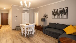 A modern living room with a dining area, a gray sofa, and a wall-mounted clock. - Appartamento Adara by Wonderful Italy (Bari)