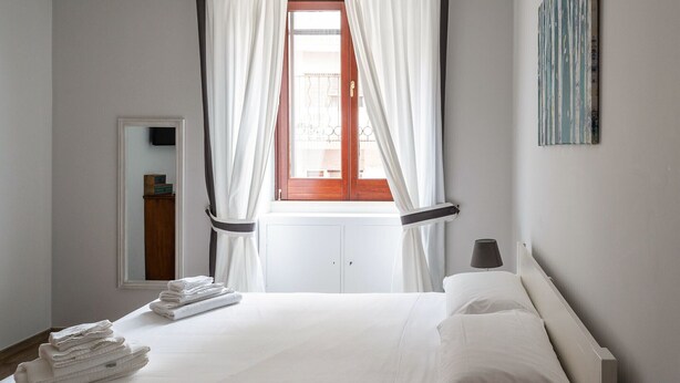 A hotel room with a bed, a window with curtains, a bedside table with a lamp, and a wall-mounted artwork. - Appartamento Adara by Wonderful Italy (Bari)