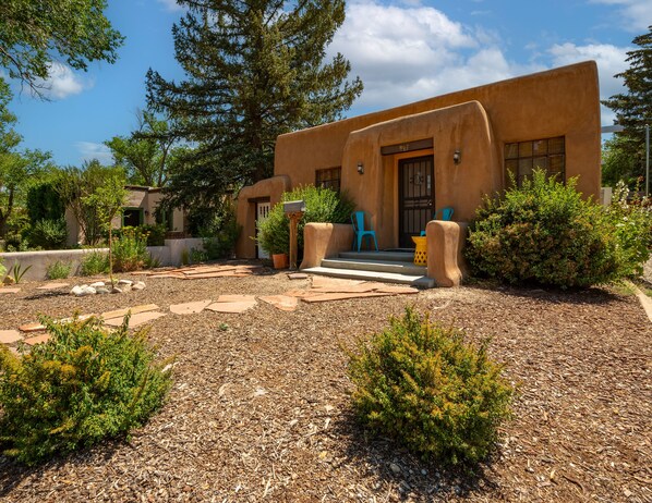 A stucco building with a mailbox, two blue chairs, and a small garden with mulch and plants. - Authentic Charm with Modern Comforts (Santa Fe)