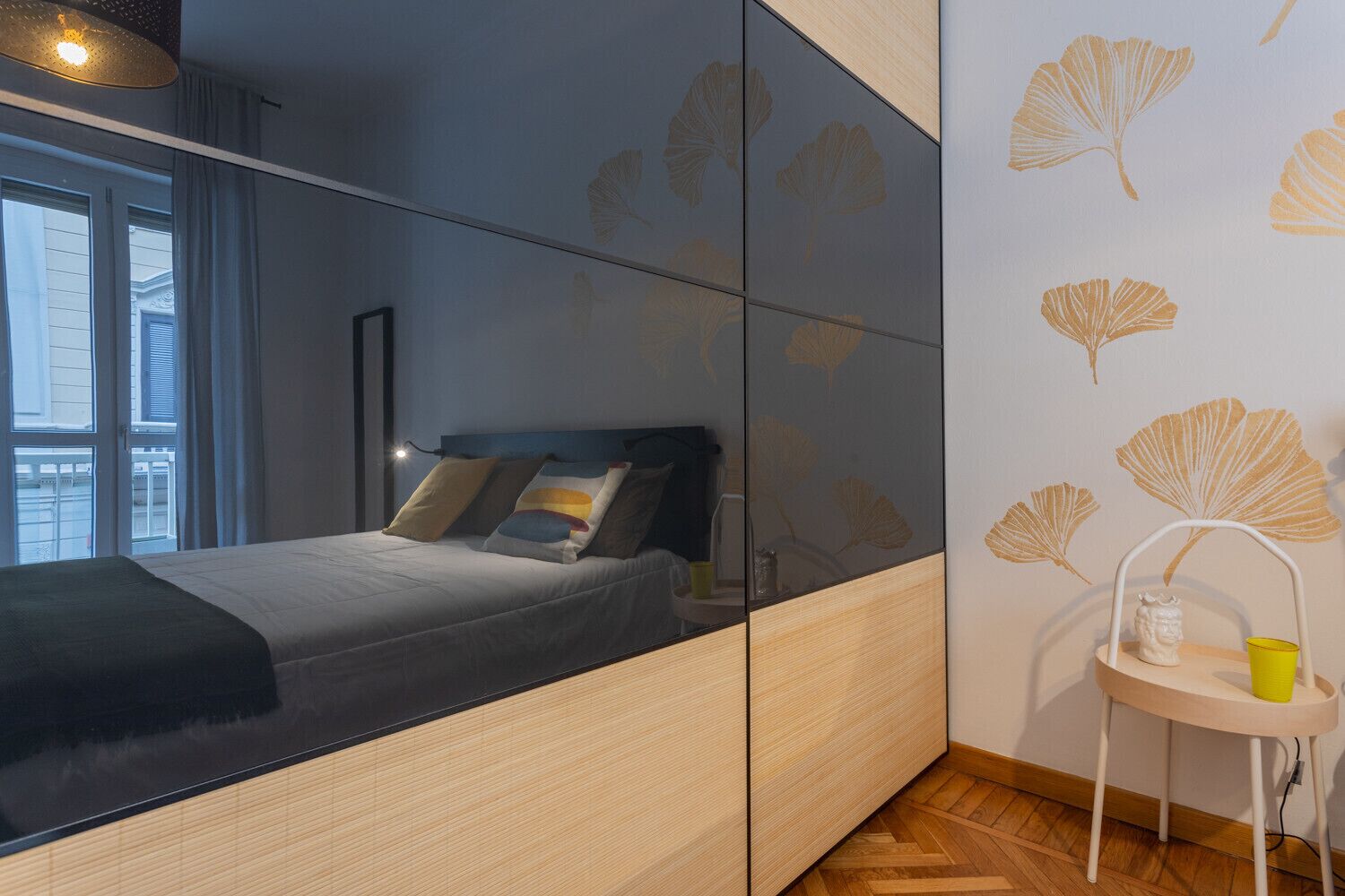 A modern bedroom with a bed, bedside table, and a mirror.