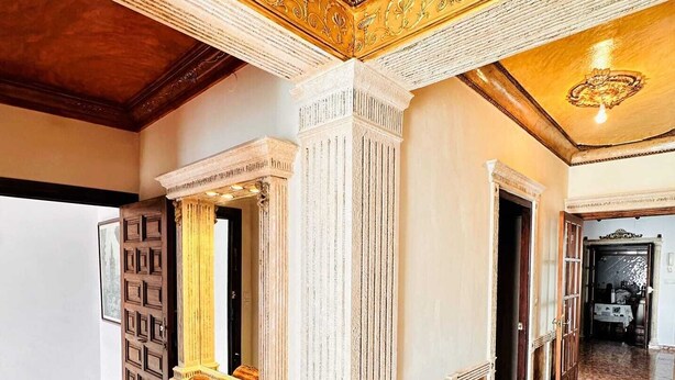Amplia habitación con piso de mármol, un espejo grande y decoraciones ornamentales en el techo.
