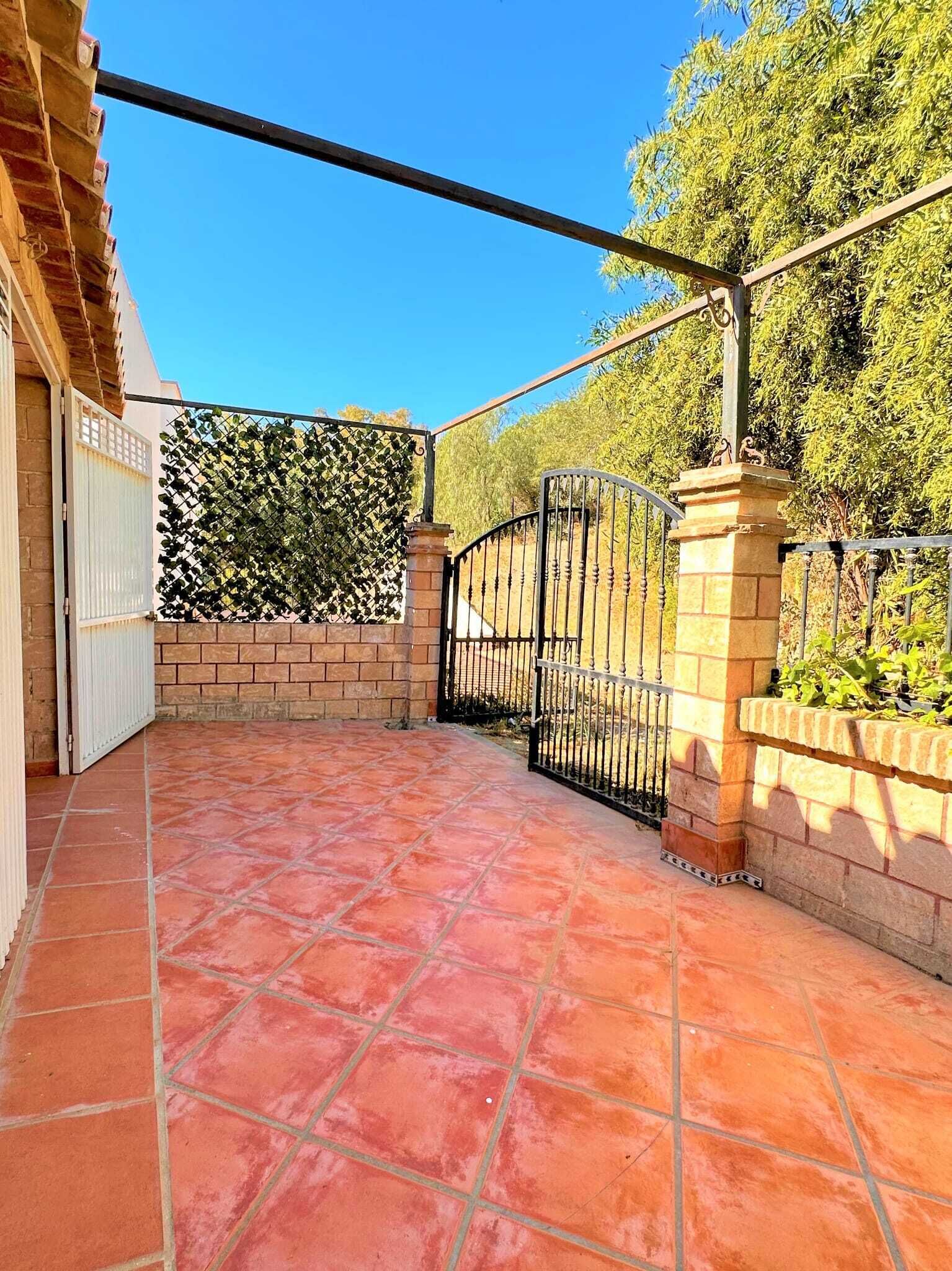 A covered patio area with red tiles, a metal gate, and a brick wall.