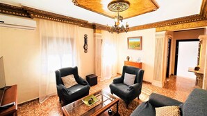 Una sala de estar con dos sillones, un sofá, una mesa de centro de vidrio y una araña.