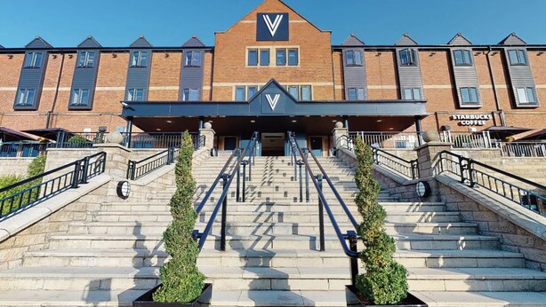 Un edificio de varios pisos con un llamativo logo en forma de 'V' en la fachada, un letrero de Starbucks Coffee y un conjunto de escalones de piedra que conducen a la entrada.