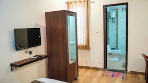 A room with a TV mounted on the wall, a wooden wardrobe, a bathroom with a toilet and shower, and a small rug on the floor. - Hotel Dream villa udaipur  (Udaipur)