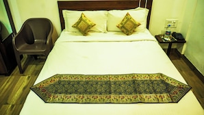 A hotel room with a bed, two pillows, a chair, a nightstand with a phone and water bottle, and a decorative rug. - Hotel Dream villa udaipur  (Udaipur)