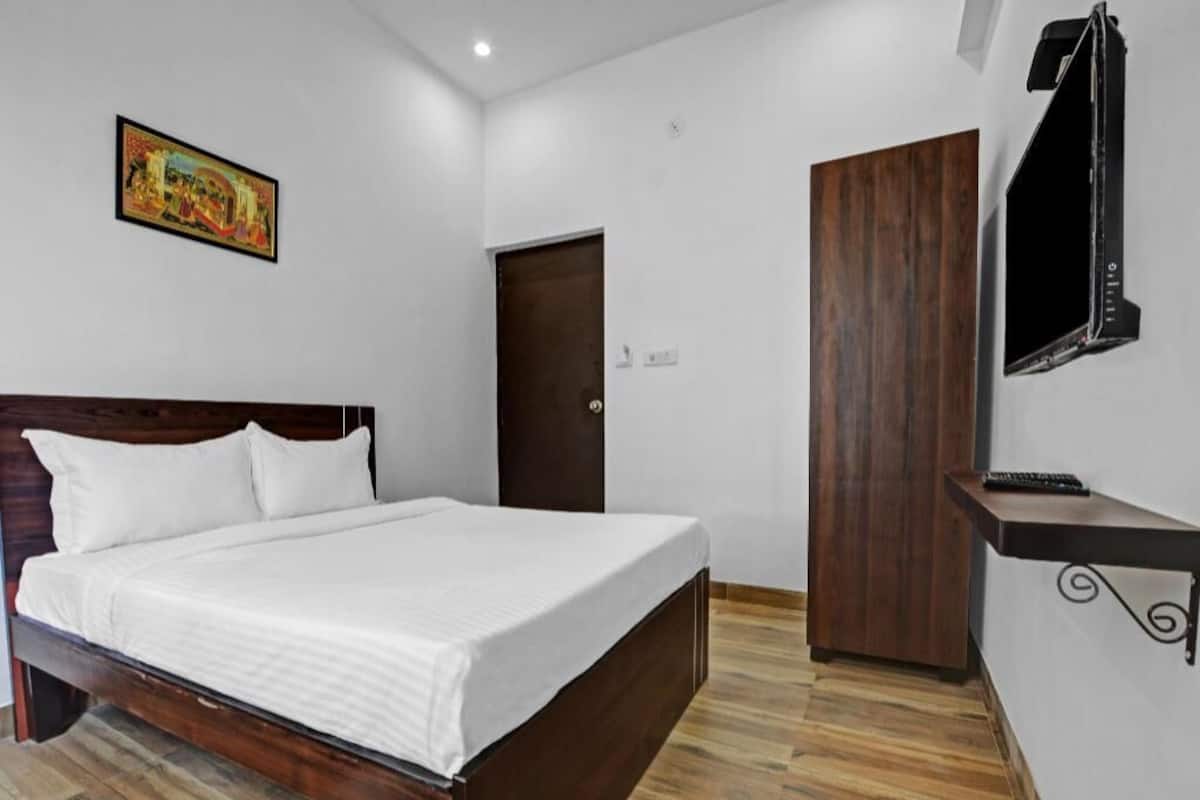 Una habitación de hotel con una cama de madera, un televisor montado en la pared, una puerta y un estante pequeño.
