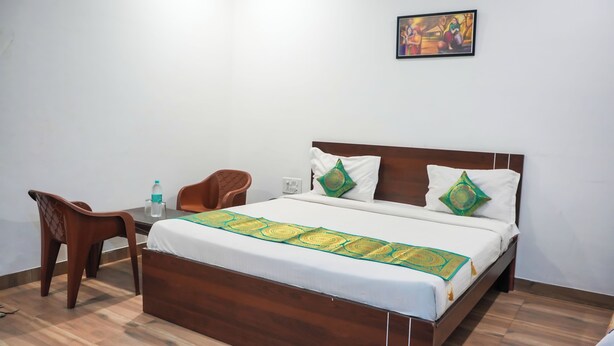 A neatly made bed with a patterned bedspread, a wooden headboard, and two decorative pillows. A small table with a chair and a water bottle is beside the bed. - Hotel Dream villa udaipur  (Udaipur)