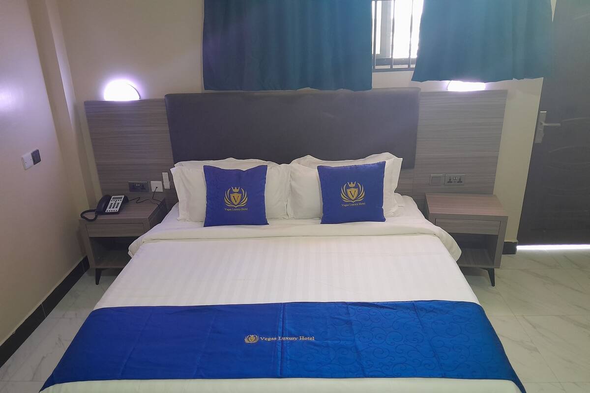 Une chambre d’hôtel comprenant un lit, deux oreillers ornés d’un logo, une table de chevet avec un téléphone et une petite table de nuit.