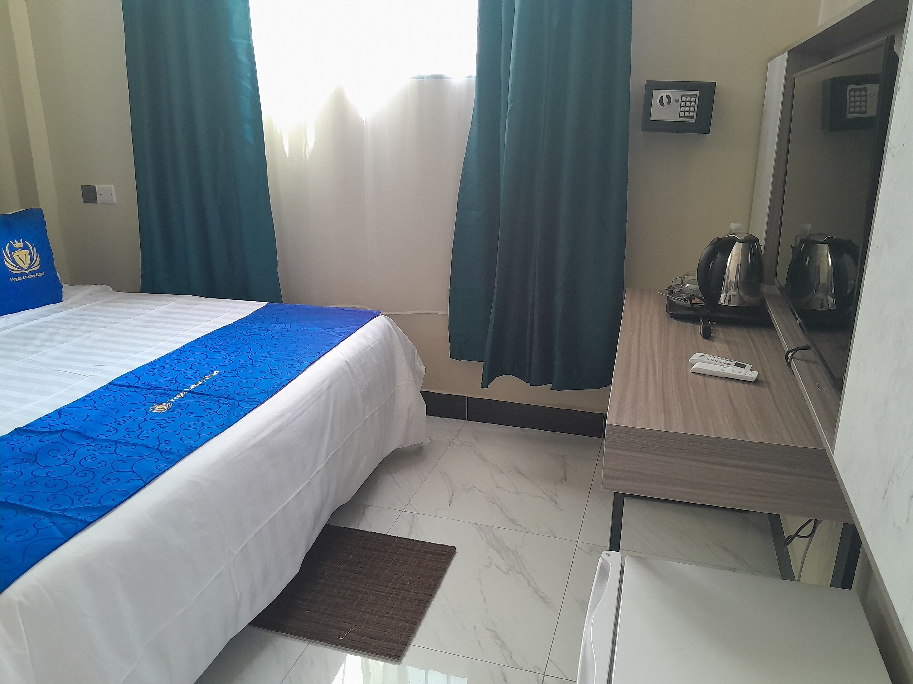 A hotel room with a bed, a desk, a mirror, a kettle, and a remote control.