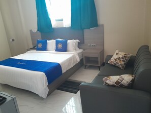 A hotel room with a bed, a nightstand, a sofa, and a window with curtains.