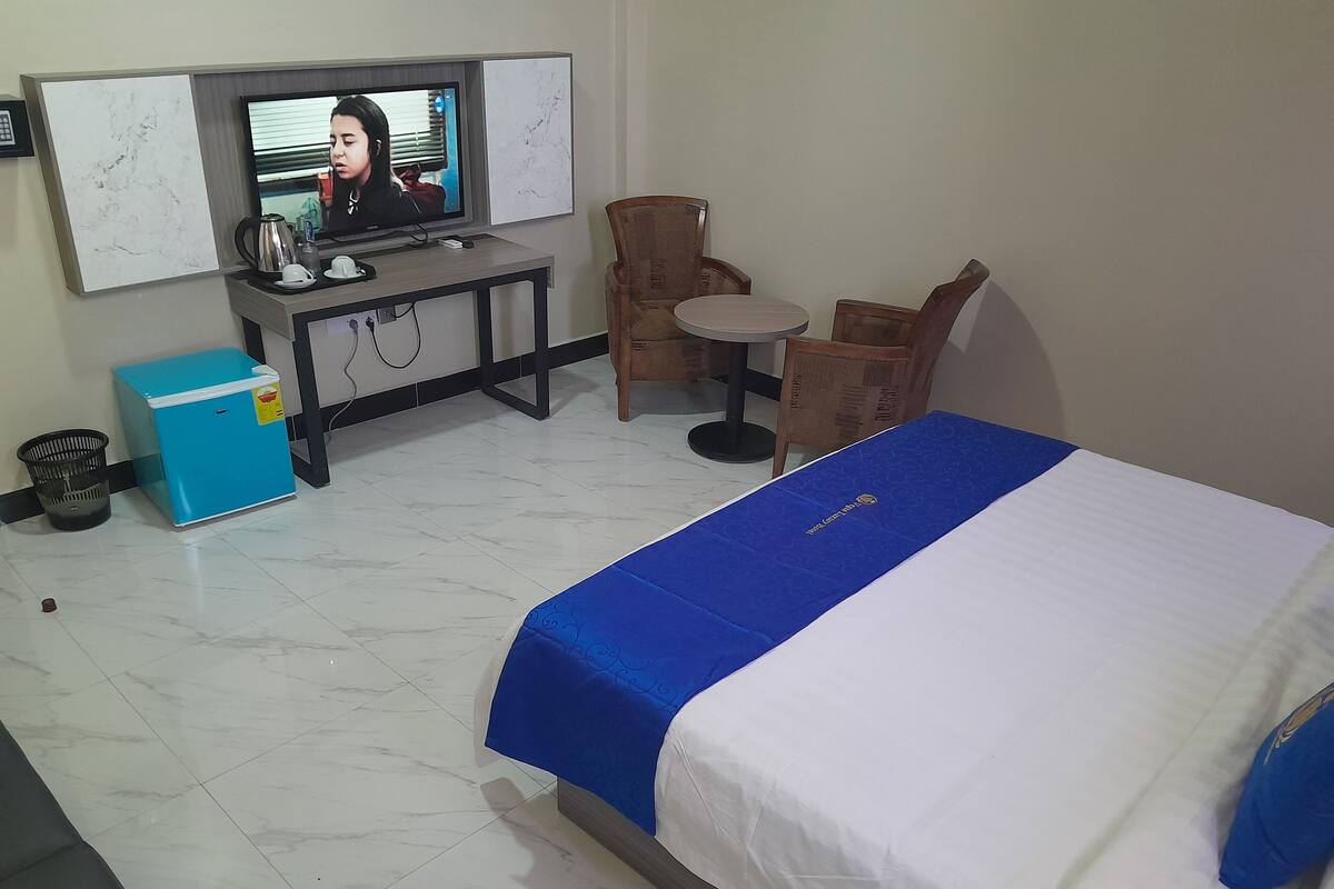 Une chambre d’hôtel comprenant un lit, un bureau avec une télévision, un petit réfrigérateur, une chaise et une poubelle.