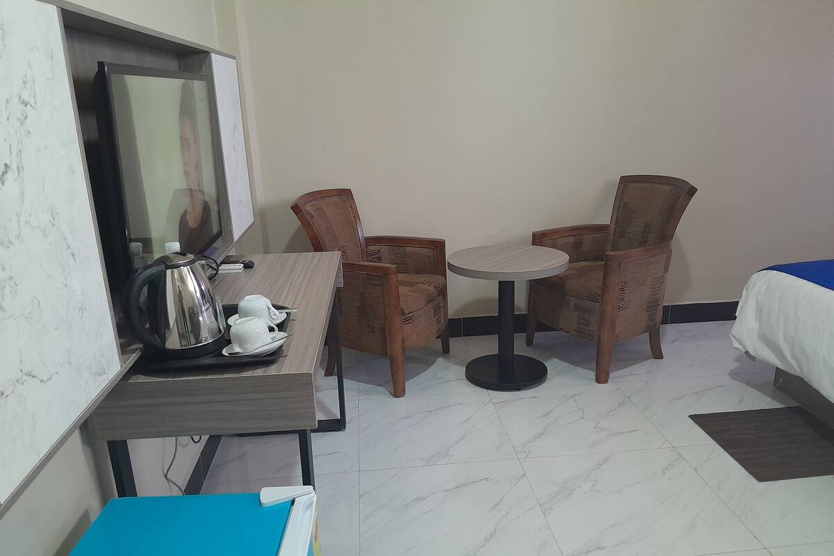 Une chambre d’hôtel avec un lit, une petite table ronde avec des chaises, une machine à café et un buffet bleu.